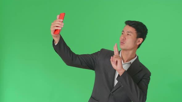 The Smiling Asian Business Man Making Selfie While Standing On Green Screen In The Studio