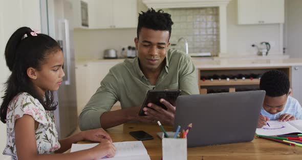 African american father, daugher and son sitting at kitchen table doing homework