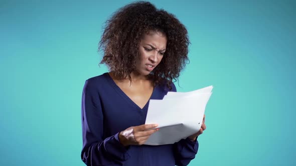 Serious african woman is unsatisfied with papers, bills, documents or reports on blue 