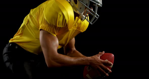 American football player bending holding a ball on turf with both his hands