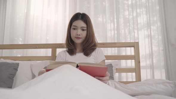 Beautiful young Asian woman reading a book while lying on the bed when relax in the morning.