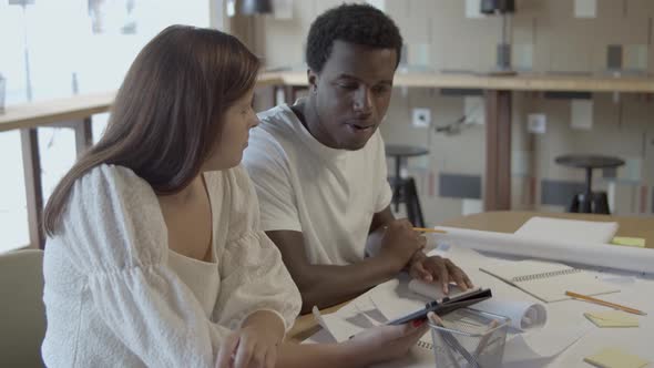 Young Designers Sitting at Table with Tablet and Blueprint