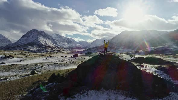 Male mountain climber raising hands with icepick on top of snowy peak