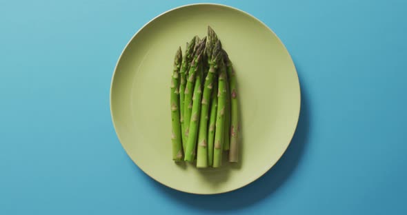 Video of fresh asparagus on green plate over blue background