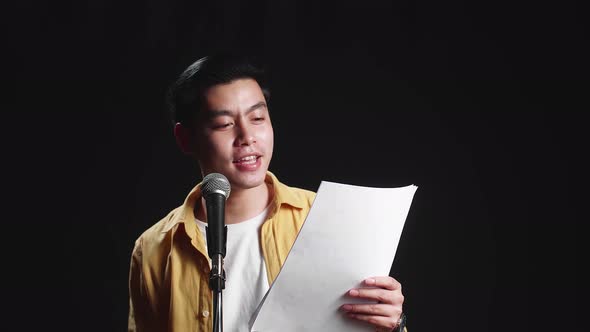 Asian Man Singer Holding White Paper And Singing Into Microphone On Black Background