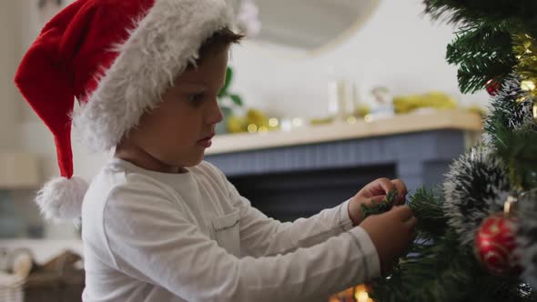 Caucasian boy wearing santa hat decorating christmas tree