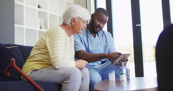 Video of african american male doctor using tablet with caucasian senior woman