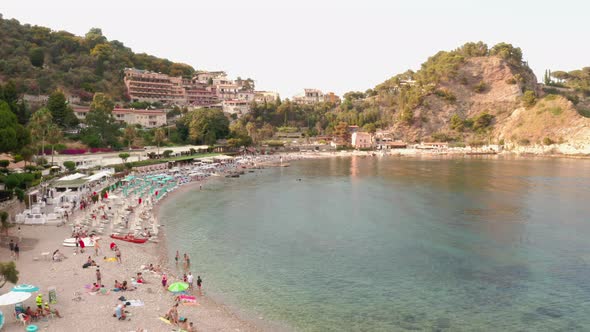 Bird's eye view of a crowded sandy beach by the clear Mediterranean Sea. Taormina, Sicily, southern