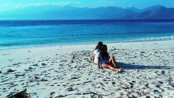 Tourists happy and smiling on idyllic coastline beach trip by blue ocean with bright sandy backgroun