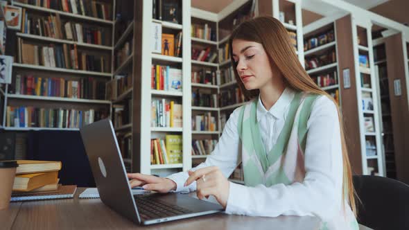 Female using laptop browsing internet in library alt