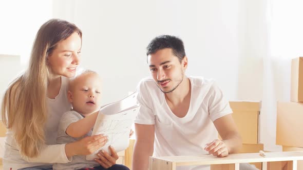 Happy Young Family with Little Boy Reading Instruction and Assemble Furniture Together at Living