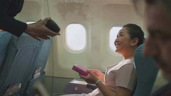 Asian woman sitting in airplane buying onboard product from air hostess and paying by credit card.