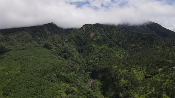 Aerial view of flying in a tropical forest, mountain, and valley in Indonesia.