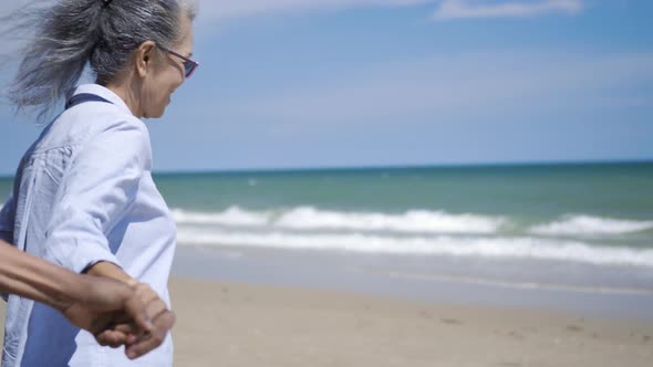 senior man and woman couple holding hands walking to the beach sunny with bright blue sky