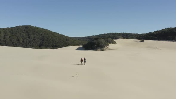 Aerial view of couple walking in sand dunes.