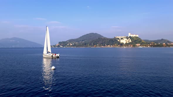 White sailboat sailing on Lake Maggiore waters in Italy with Angera castle in background