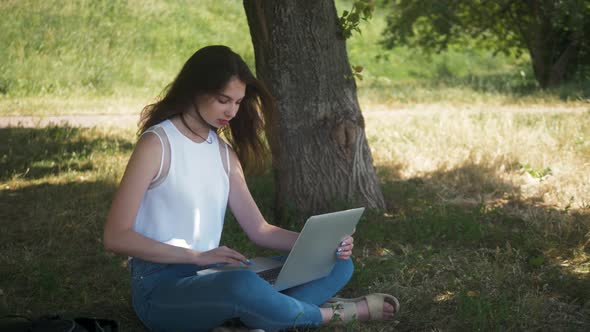 Smiling Woman Student Sitting on Bench Outdoors at the Street, Using Laptop Computer, Use Mobile