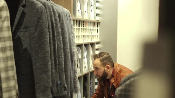 Stylish Young Man In The Store Looks At The Shirts On The Store Shelf. He Makes Purchases.