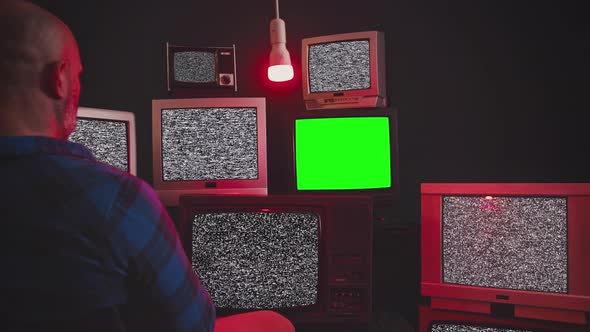 A Man Sits in Front of Group of 9 Vintage TV with Chroma Key Screens in Room with Black Wall