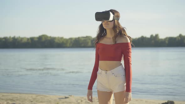 Surprised Young Caucasian Woman in VR-glasses Looking Around Outdoors. Portrait of Excited Brunette