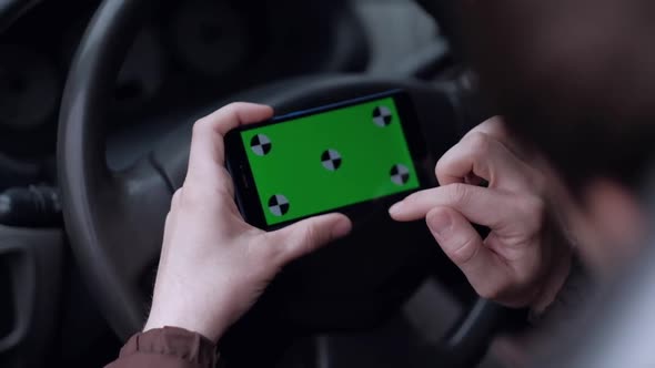 Male driver using smartphone  with green screen in the car.