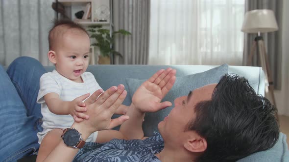 Asian Father And Son Playing On Sofa In Home