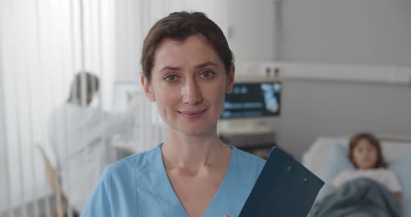 Happy Female Nurse Smiling at Camera Standing in Pediatrics Hospital Room