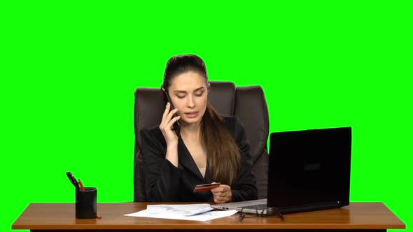 Business Woman at the Workplace Takes a Credit Card and Call on the Phone. Green Screen. Studio