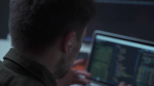 The Programmer is Working at a Computer and is Negotiating Wirelessly with a Small White Earpiece in