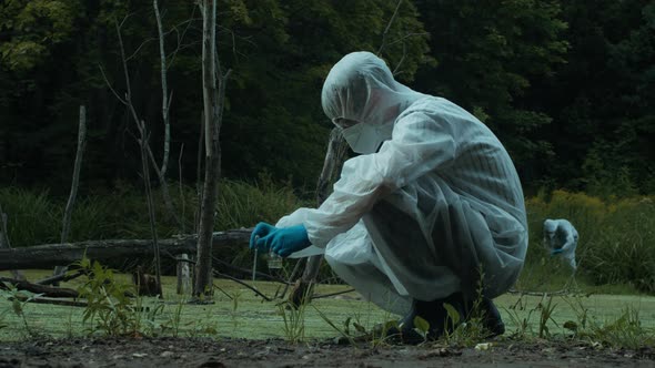 Chemist in Ppe Taking Water Analysis From Swamp Using Flask and Pipette Wearing Protective Suit and