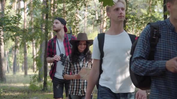 Row of Cheerful Young Caucasian Men and Women Strolling in Summer Forest and Leaving. One Tourist