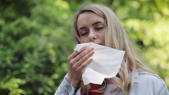 Young Woman with with Allergy Symptom Blowing Nose Standing in the Park. Sick Girl Sneezing and