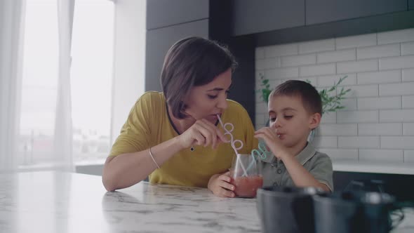 Young Mom and Son Drinking Juice with Candy at Kitchen