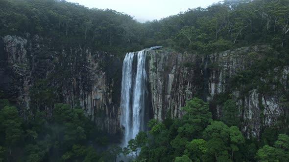 Panoramic view of a majestic waterfall spilling down a tropical rainforest covered mountain.  Drone