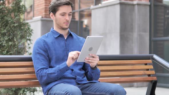 Man Cheering for Success on Tablet while Sitting on Bench