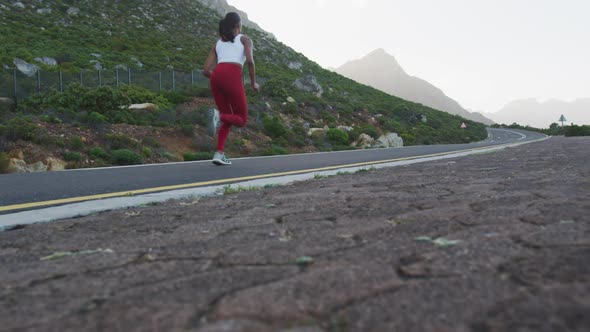 Fit mixed race woman exercising running on a country road near mountains