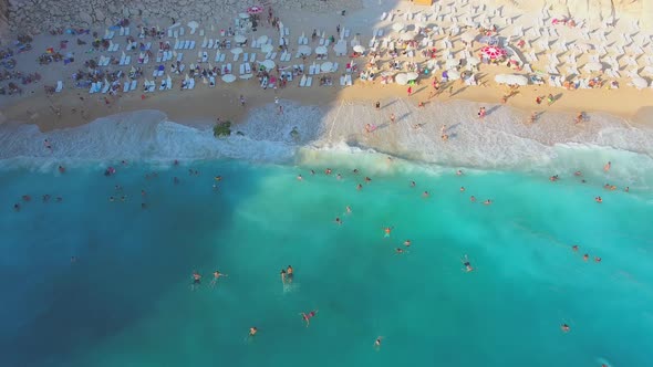 People Swim on Light Blue Sea in the White Sandy Beach Near the Rocky Mountainside