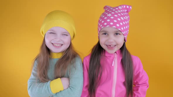 Two Cheerful Cute Little Girls Having Fun on a Yellow Background