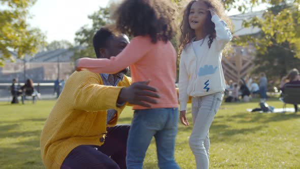 Happy Afro Young Father Giving High-five To Cute Preschool Daughters and Hugging Outdoors