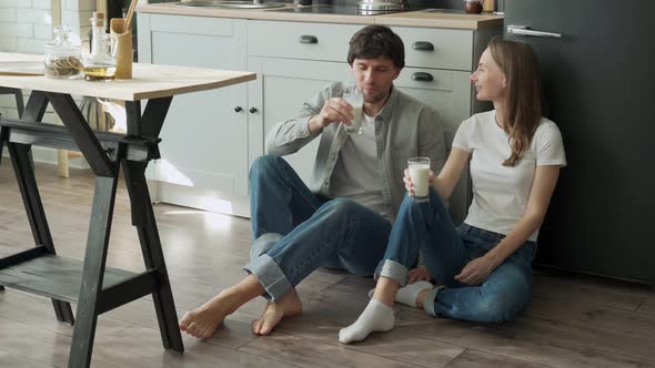 Young Couple Sits on the Floor of Their Kitchen and Drinks Delicious Milk