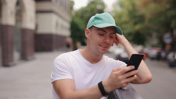 Man in Cap Using Smartphone at Summer City