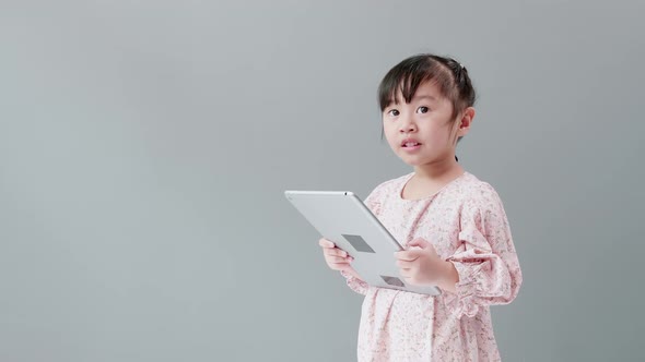 Little asian girl looking at camera, looking on tablet and smiling in studio.