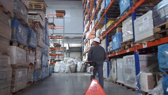 A Man Carries a Lift for Pallets in a Logistic Warehouse