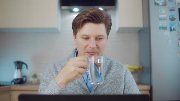 Man Drinks Water While Working at a Laptop