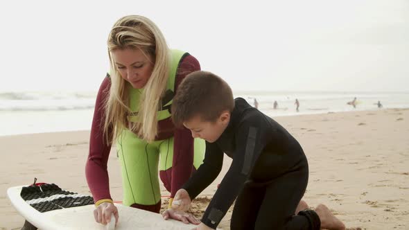 Mother and Son Waxing Surfboard on Beach