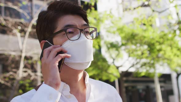 Asian man wearing face mask talking on smartphone on the street