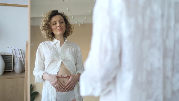 Pregnant Woman Looking In Mirror While Holding Her Belly