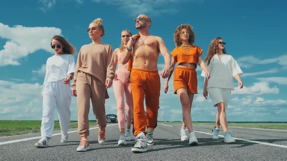 A Group of Brutal Stylish Hipsters Are Walking Along the Road Against the Background of the Summer