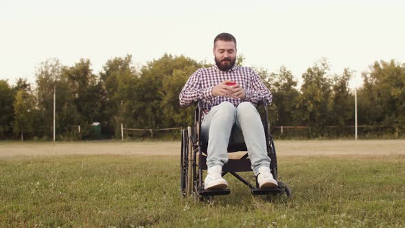 Disabled person hipster man is sitting in wheelchair in public park outdoor, drinking coffee