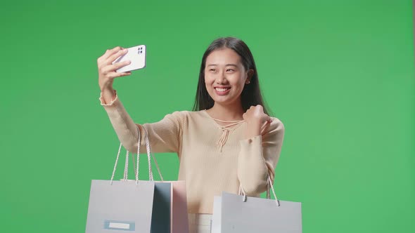 Woman With Shopping Bags Having Video Call On Mobile Phone While Standing In Front Of Green Screen